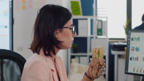 entrepreneur woman eating tasty sandwich during takeout lunchbreak working at financial graphs