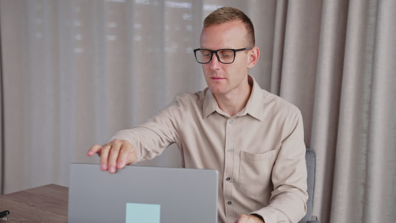 Male employee wearing glasses works on his laptop. Man puts off glasses, closes laptop, takes phone and comes up to female colleague drinking coffee.