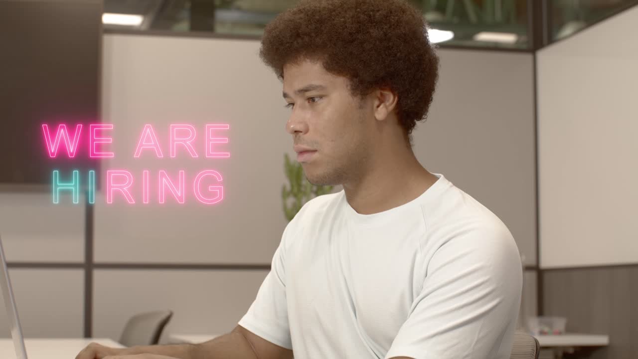 Young Black male on a computer with We Are Hiring overlay graphic.