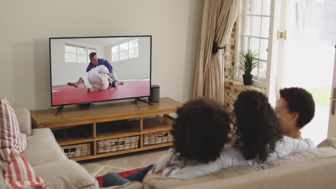Famiglia felice seduta a casa insieme che guarda un incontro di judo in TV