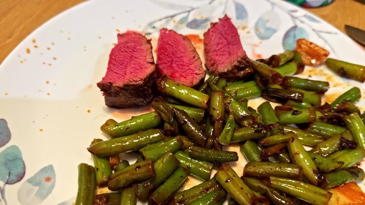 Three slices of medium-rare steak served alongside sautéed green beans on a floral-patterned plate. Perfect for culinary blogs or cooking tutorials