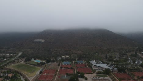 thick fog progressively descends, obscuring a hill, a sports center with tennis courts, and a swimming pool