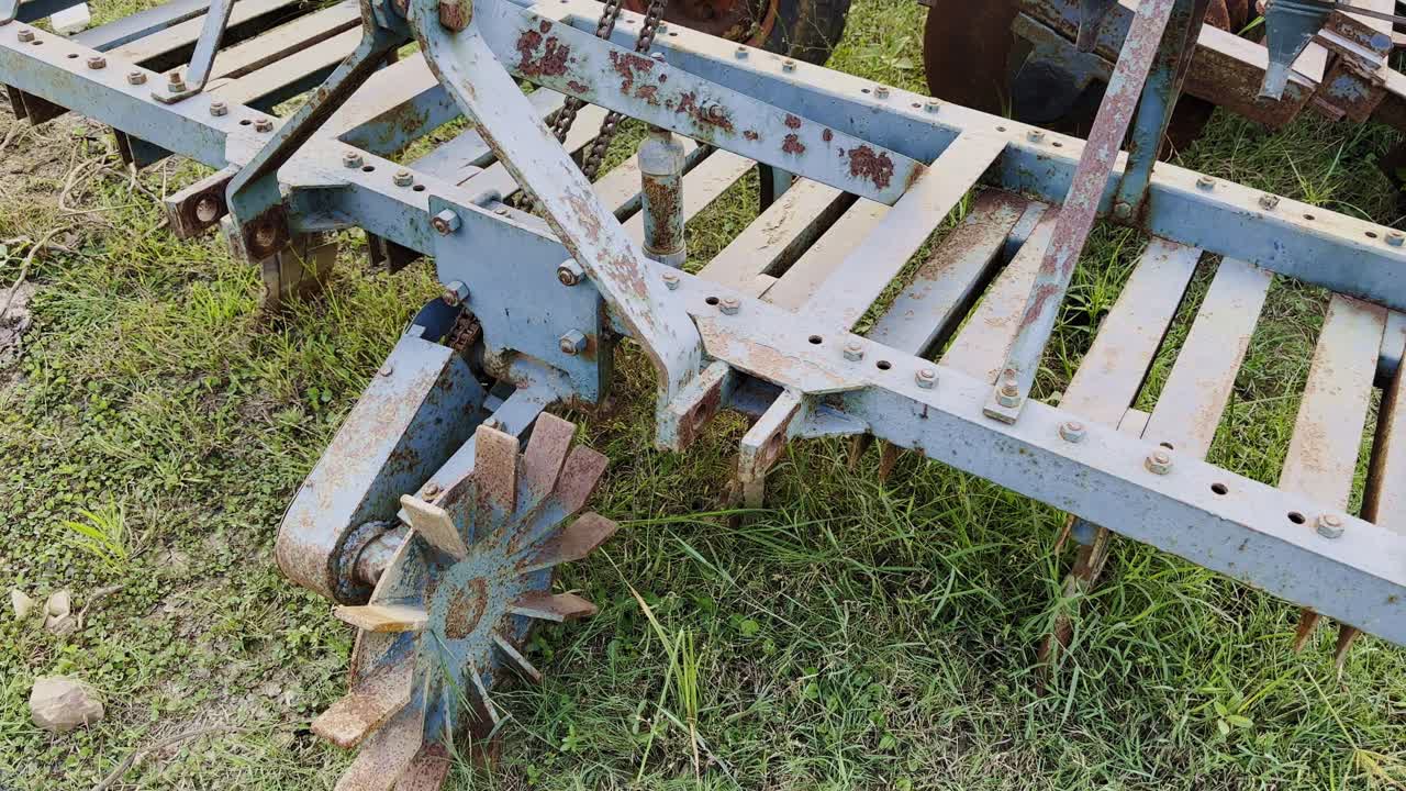 Wide-angle shot of old rusty farm equipment resting on grassy ground, showing weathered metal textures and the charm of rural agricultural machinery