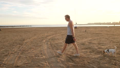 Hombre-Caminando-Por-Una-Playa-Mediterránea-Con-Su-Perro-Al-Atardecer