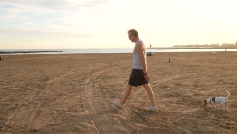 man walking along a mediterranean beach with his dog at sunset