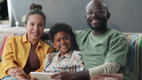 retrato de una familia afroamericana sonriente con una tableta en el sofá en casa