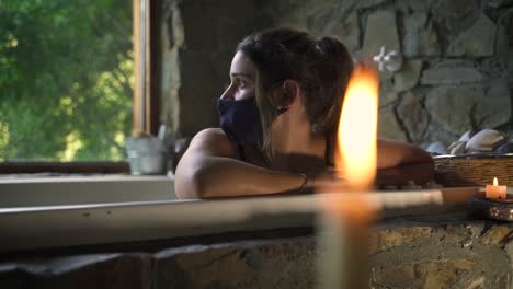 Mujer-Joven-Y-Atractiva-Que-Se-Da-Un-Baño-Elegante-En-Un-Jacuzzi-Con-Máscara-Covid-Esperanza-Con-Una-Gran-Ventana-De-Naturaleza-Verde-Capaz-De-Cámara-Lenta-60fps