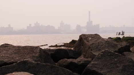 view of manhattan covered in smoke from wildfires seen from beach on the east river with rocks in the foreground