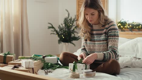 Caucasian-woman-sitting-on-bed-and-packing-Christmas-gift-at-home