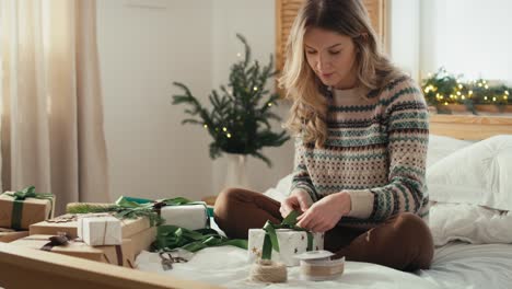 mujer caucásica sentada en la cama y empaquetando regalo de navidad en casa