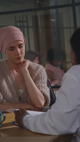 vertical video of serious young woman patient wearing headscarf undergoing chemotherapy treatment for breast cancer meeting with oncologist or doctor in hospital