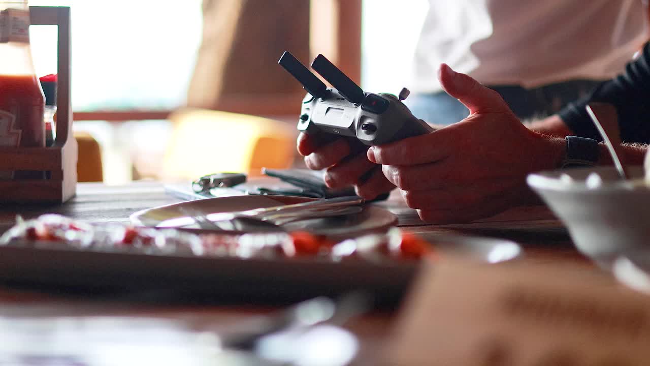 Hands operate a drone controller in a restaurant with natural lighting, capturing a relaxed, focused atmosphere in Phuket, Thailand