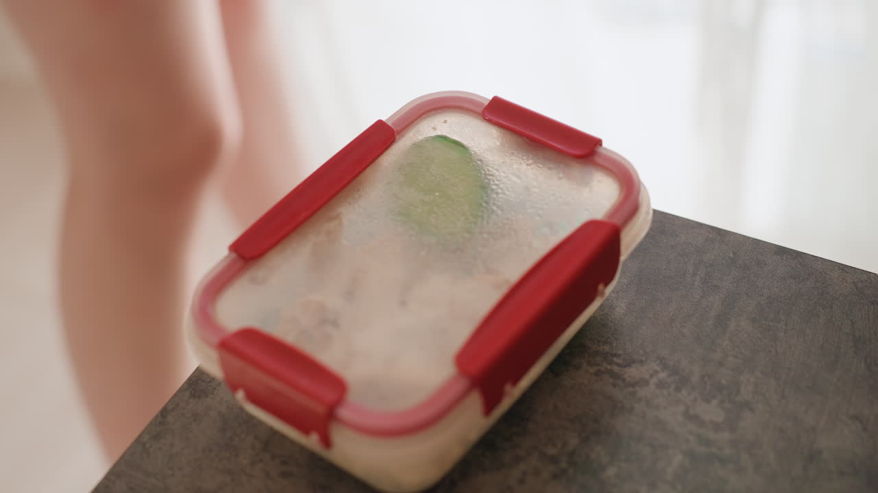 Woman Carrying Lunch, Woman Lifts Sealed Lunchbox Early, Woman Transports Sealed Meal Toward Room In Morning Light, Daily Morning Activity Involves Woman Lifting Sealed Lunchbox Towards Her Room