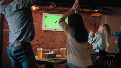 un grupo de amigos en el pub mirando la pantalla verde de la televisión saltan de sus asientos y se regocijan en felicitarse mutuamente. ver fútbol ver hockey baloncesto. aficionados ver el partido de la copa del mundo