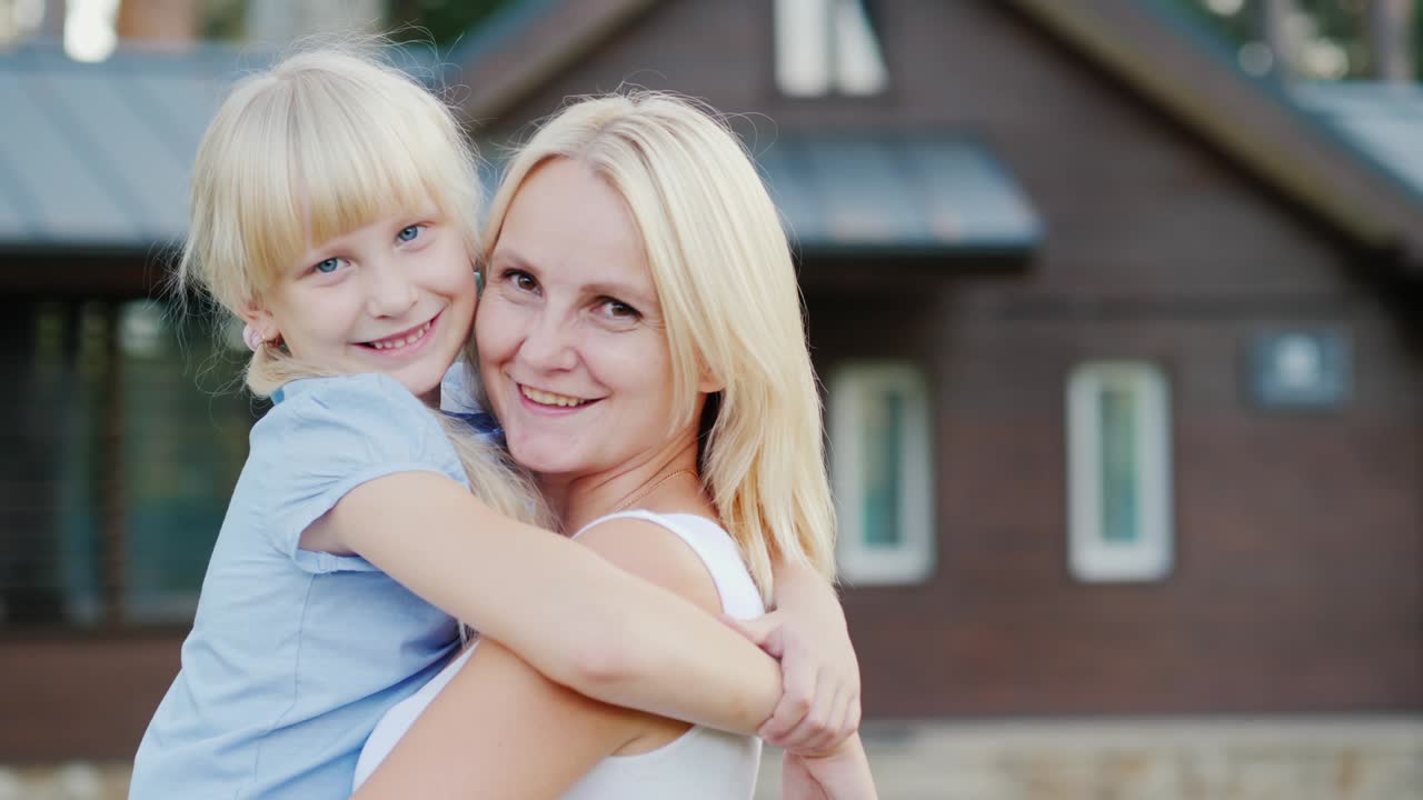 Porträt einer Mutter mit einer kleinen Tochter, die sich vor dem Hintergrund ihres neuen Zuhauses umarmen und in die Kamera blicken. Konzept - Einweihungsfeier