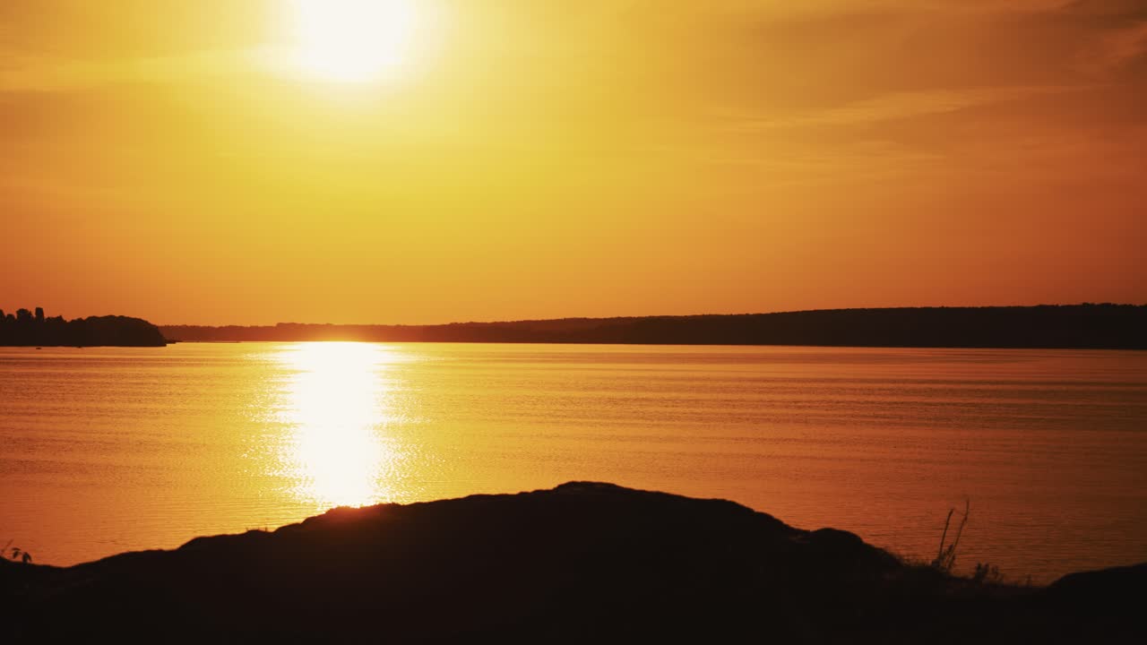 Amazing view of a golden sunset path over water surface and a biker. Silhouette of a male biker in helmet rides up to the river during the setting sun.