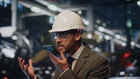 el jefe furioso gritando teléfono inteligente en el taller de producción en casco de cerca.