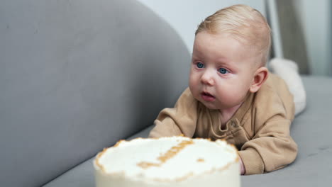 blue-eyed baby boy lying in front of a cake. four months old infant lies on his belly. close up.
