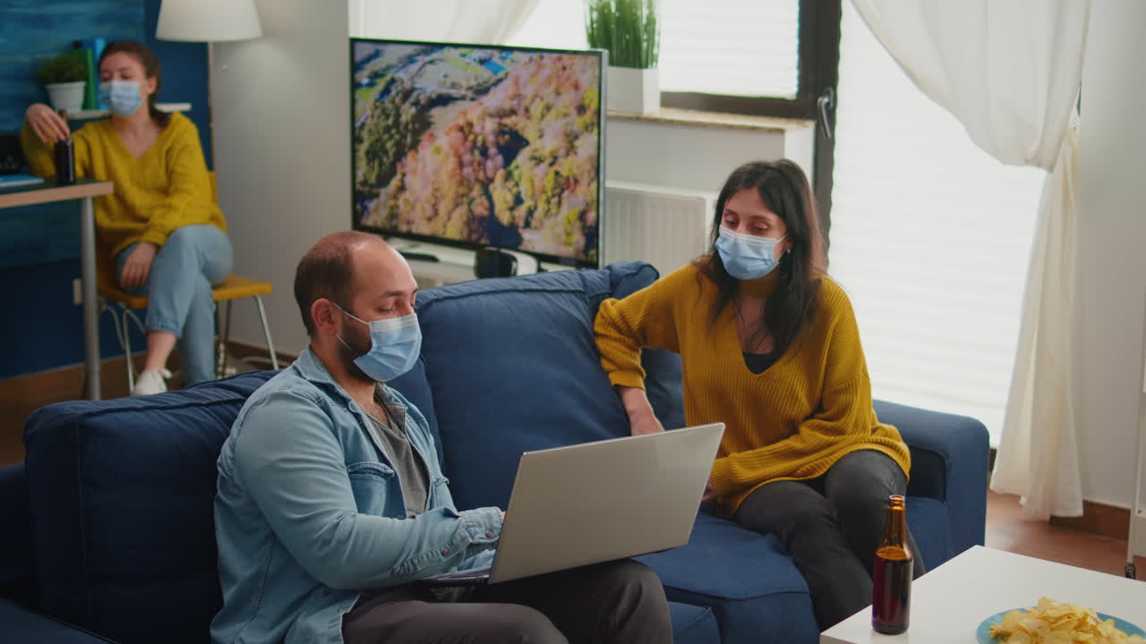 Man with mask showing new movie on laptop to woman