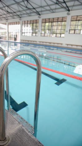 vertical video: empty indoor swimming pool with lane dividers and metal ladder