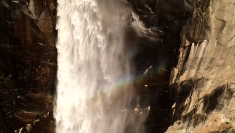 una pintoresca belleza de velo de novia cae a medida que cae en cascada y se desliza hacia abajo, con un arco iris tomando forma dentro del agua que cae