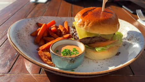 Delicious-cheeseburger-with-a-brioche-bun-and-sweet-potato-fries-with-spicy-mayonnaise-sauce,-restaurant-experience,-4K-shot