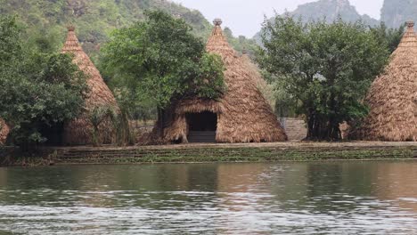cabañas de paja y árboles junto a un río tranquilo