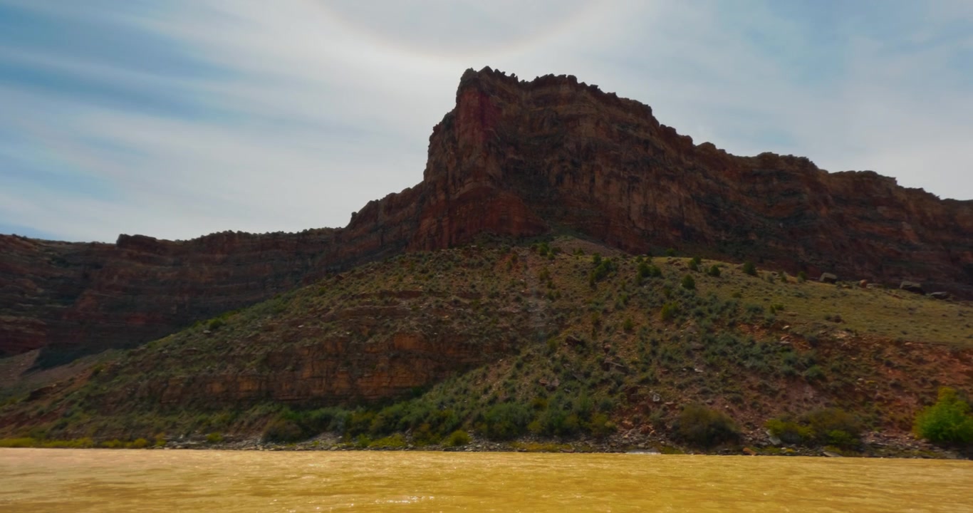 Sandsteinsbutte som rager over Yampa River-dalen under myke skyer og ørkenlys, med rødlig-oransje vann som fosser.