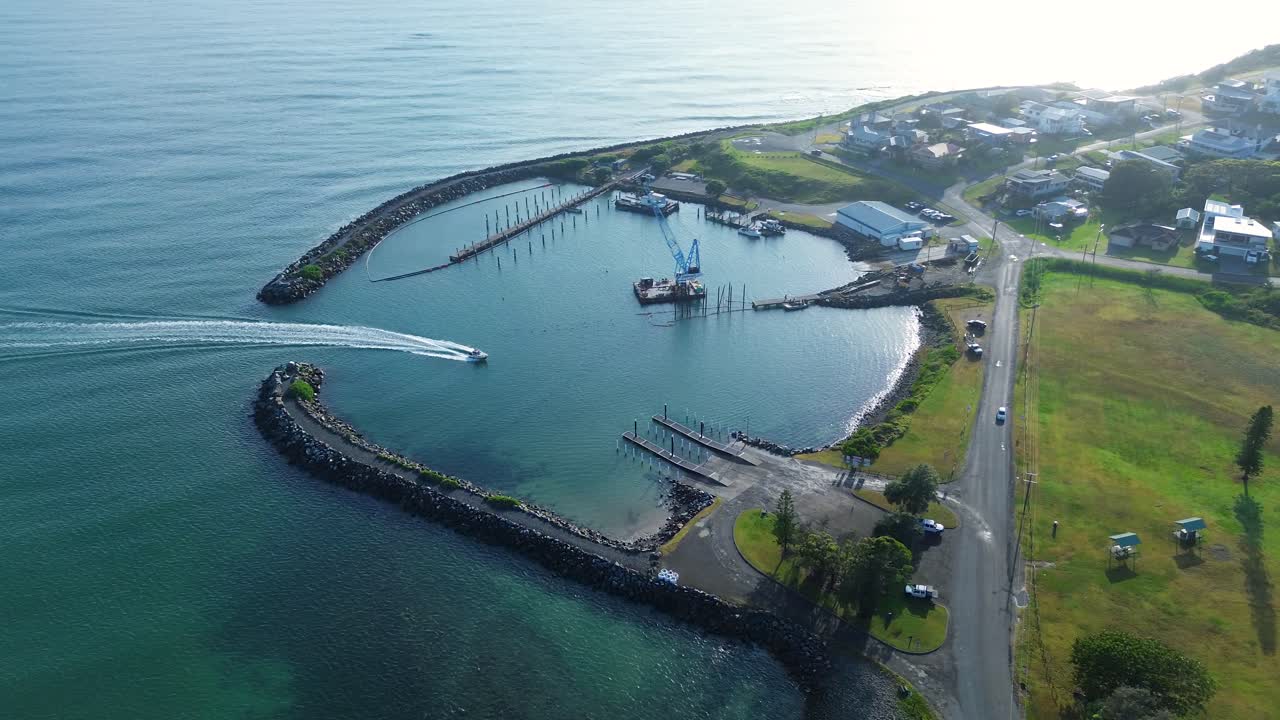 Drone aerial landscape of boat arriving in Crowdy Head Boat Harbour with wharf dock jetty and waterfront cove bay and local town suburbs main road street housing in Australia tourism infrastructure