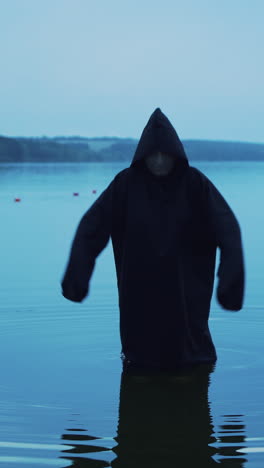evil witch in black cloak with hood in the river. halloween costume.. vertical video