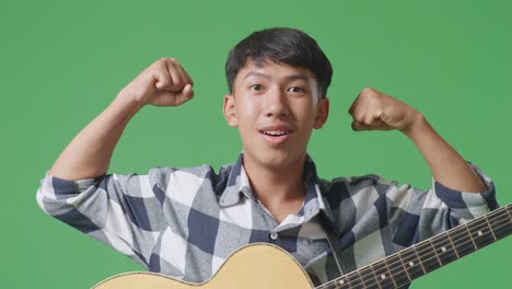 close up of asian teenager with guitar smile and flex muscle on green screen background