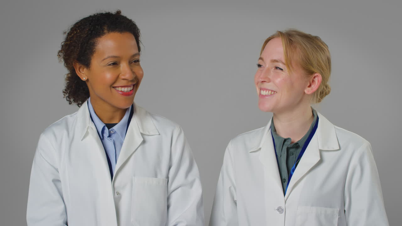 Studio Portrait Of Two Smiling Female Doctors Or Lab Workers In White Coats