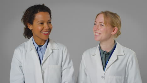 studio portrait of two smiling female doctors or lab workers in white coats