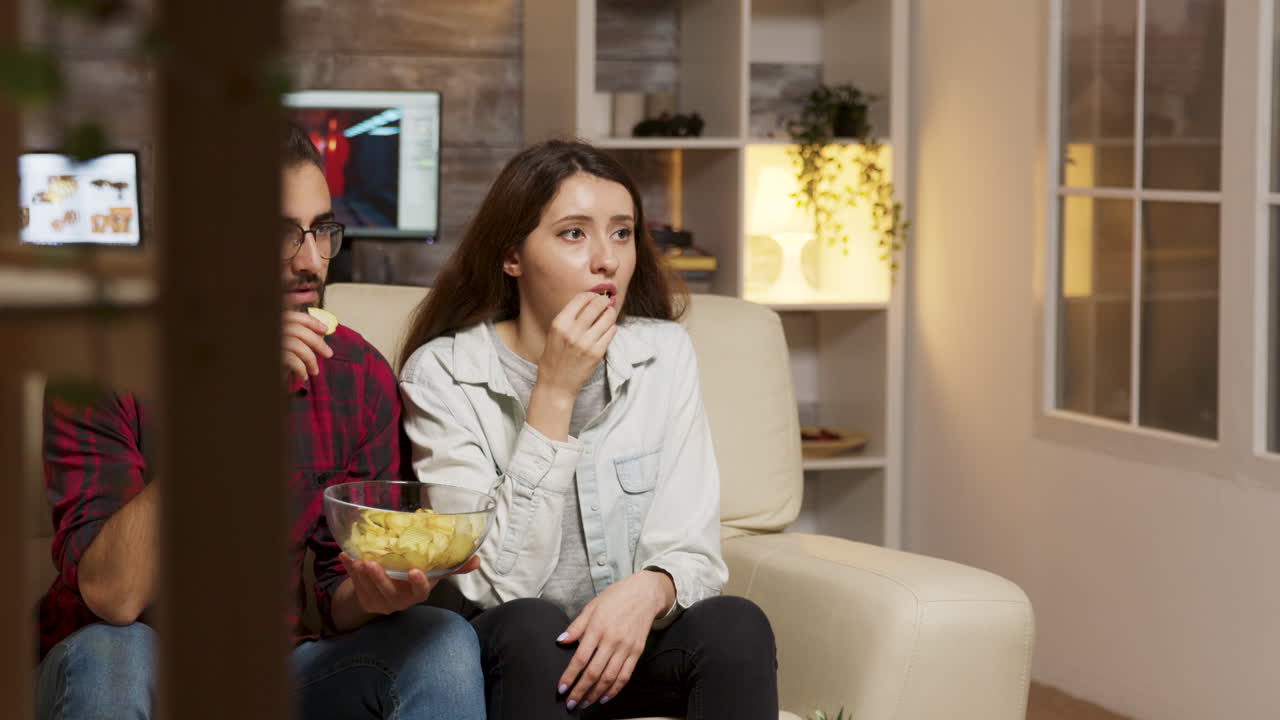 Coppia che guarda la TV e mangia patatine a casa