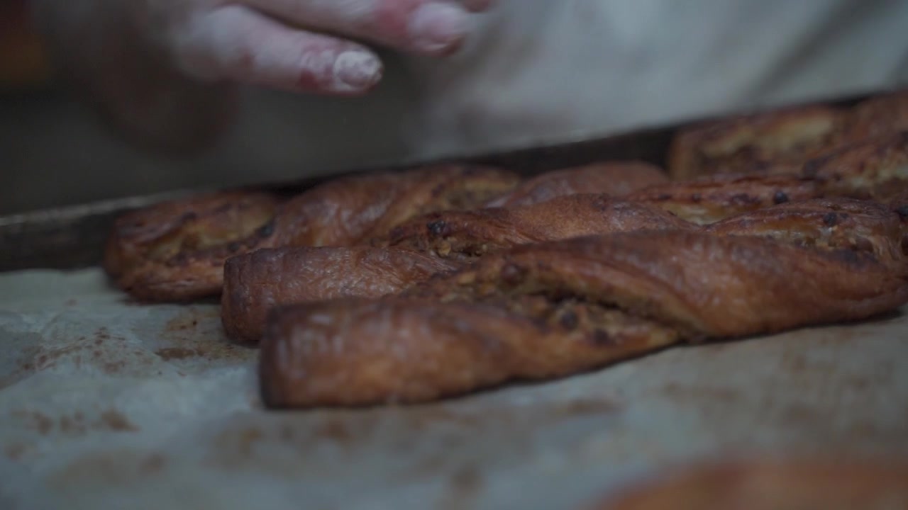 Panettiere che dispone diversi pezzi di pasticceria su una teglia in un panificio, come bastoncini di pasta o girelle