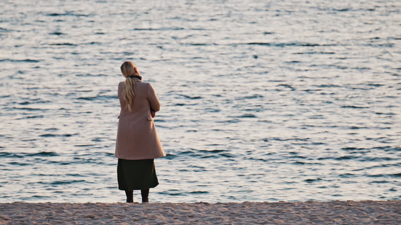 View of a blonde woman in a coat admiring the sea