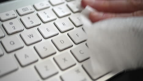 a hand cleaning dust and germs off dirty computer keyboard with an antibacterial sanitizing disinfecting wipe to keep the family home healthy and safe from contagious virus or bacteria