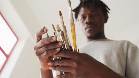 African-american-male-painter-choosing-brushes-in-artist-studio