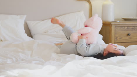 young girl playing on bed wearing pyjamas at home cuddling soft toy