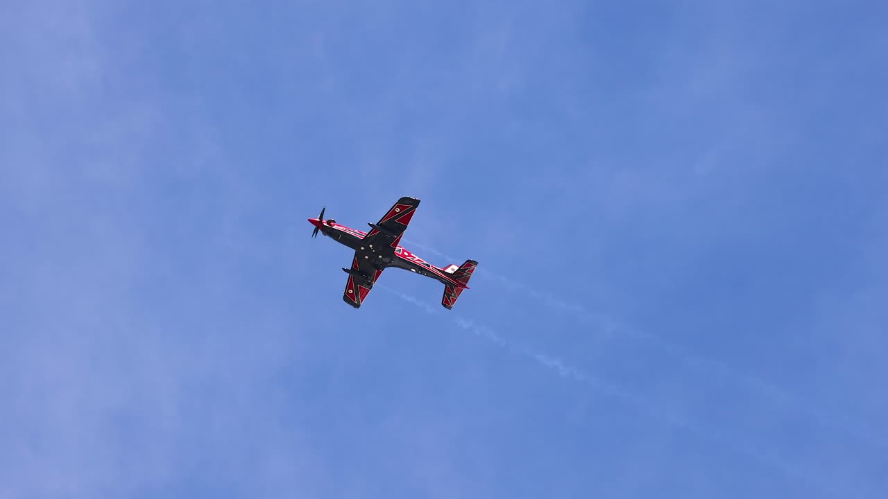 A single aerobatic plane executes impressive maneuvers against a clear blue sky, leaving white smoke trails during the Avalon Airshow