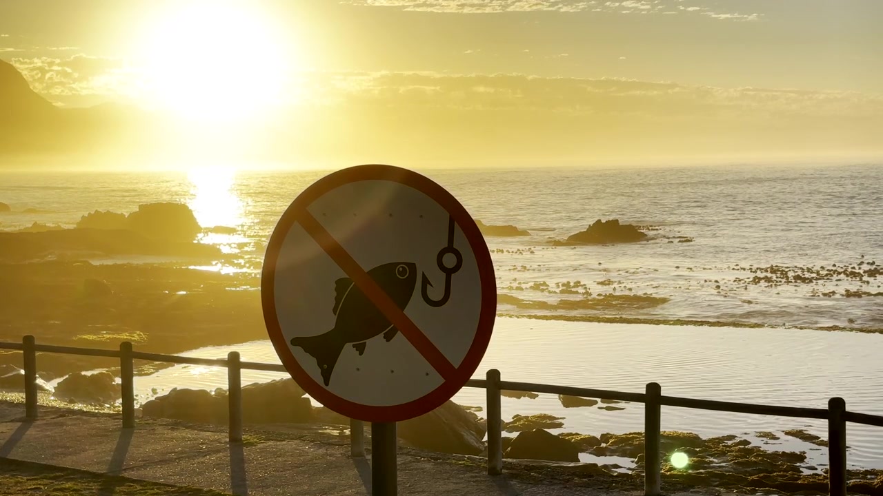 Segnale di divieto di pesca in una pozza di marea marina sulla costa, con una vivace alba sull'oceano sullo sfondo.