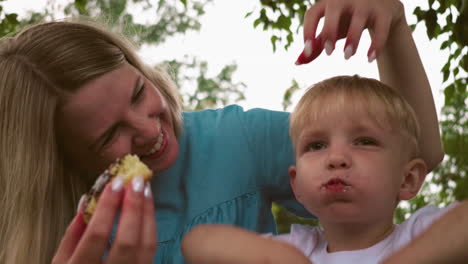 una madre alegre con una cálida sonrisa frota cariñosamente el cabello de su hijo mientras disfruta de un gran bocado de pastel