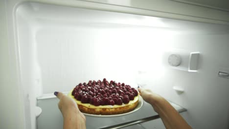 Close-Up-view-of-woman's-hands-coming-to-the-fridge,-opening-the-door-and-taking-out-the-plate-with-the-cake-decorated-with