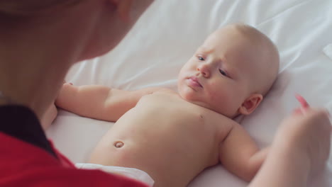 a mother playing with a 6 months old girl who is lying on a bed