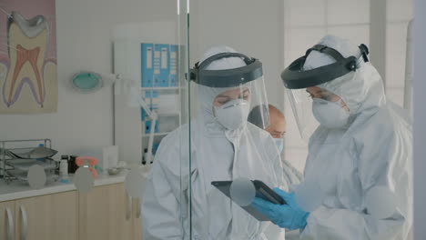 dentistry team with virus protection suits analyzing digital tablet