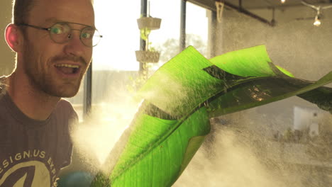 Slow-motion-footage-of-a-weird-man-spraying-water-on-a-plant-in-an-office-with-windows-in-the-background