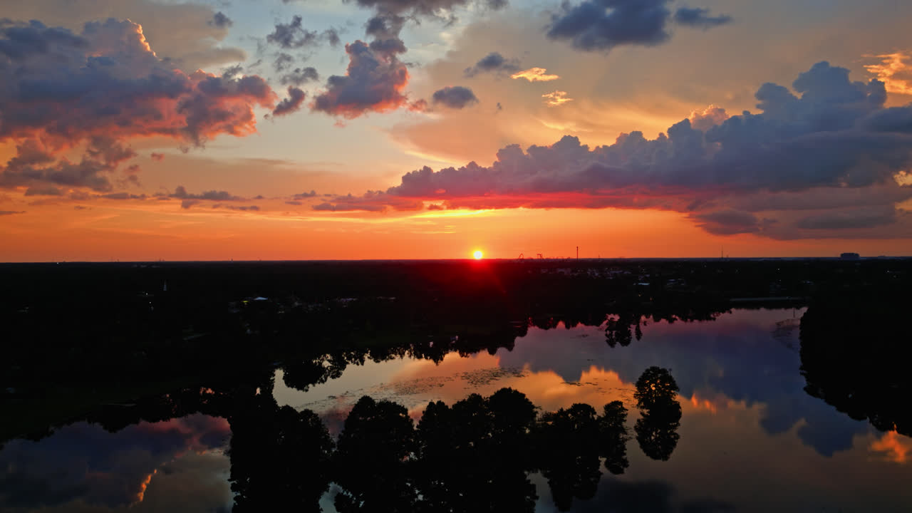 Profundos colores anaranjados y rosados del atardecer reflejados en aguas tranquilas y en la línea del horizonte de las copas de los árboles, un telón de fondo orbital aéreo celestialmente hermoso
