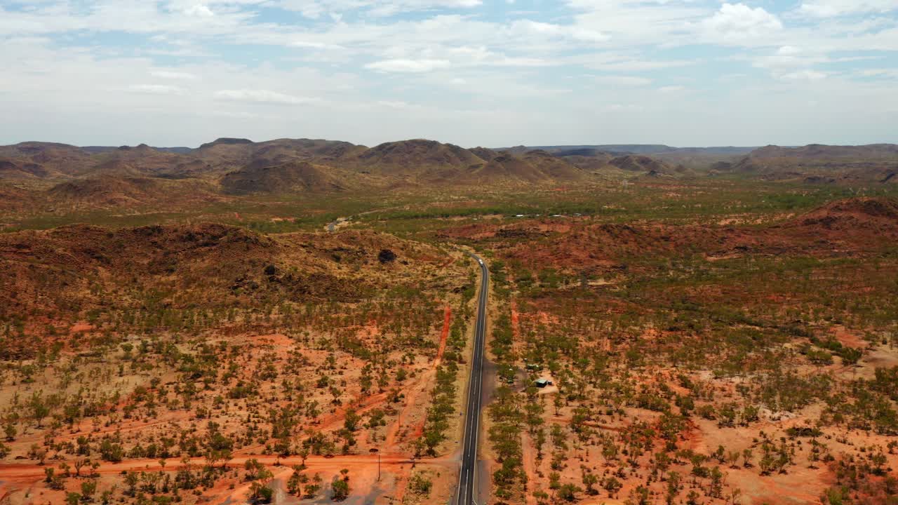Panorama della lunga strada asfaltata in mezzo alla prateria con vista sulle montagne nel Territorio del Nord dell'Australia.