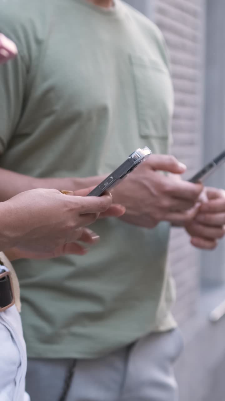Anonymous friends using smartphones while standing in city
