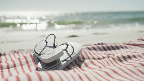 Close-up-of-flip-flops-and-towel-on-beach,-in-slow-motion,-with-copy-space